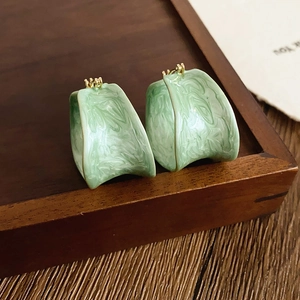Macro view of green marble texture resin hoop earrings on a dark wooden tray
