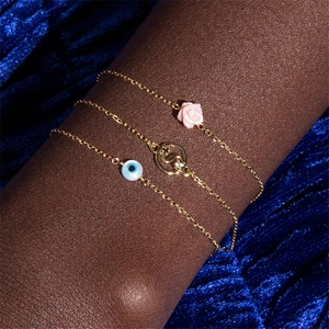 Macro detail of gold-tone evil eye and pink rose charms on a S925 sterling silver bracelet