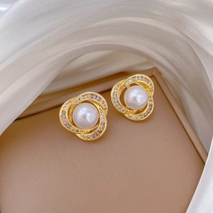 Detailed close-up of golden pearl earrings with crystal halo on white silk fabric