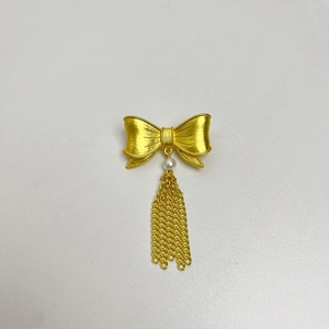 Detailed view of a gold bow brooch featuring a white pearl and metallic tassel pendant