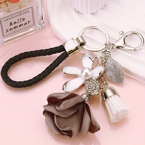 Detail of floral keychain featuring white enamel flower, pearl center and brown ribbon
