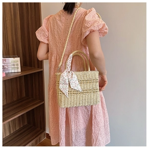 Detail of beige straw handbag with a pink floral silk scarf and woven shoulder strap