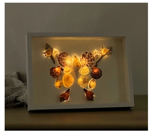 Detail of DIY seashell butterfly shadow box with warm LED lighting and white wood frame