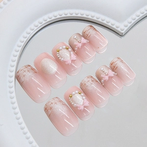 Pink cat-eye press-on nails with 3D bows, pearls, and plaid designs on a mirror surface