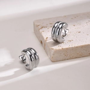 Detail of silver double-layered C-shape earrings on a minimalist beige stone base