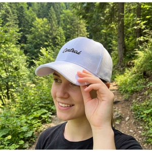 Gros plan sur une casquette blanche avec broderie Central noire dans un décor de forêt
