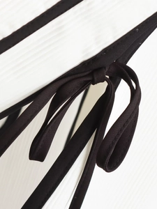 Detailed view of contrast black piping and delicate bow tie on white fabric