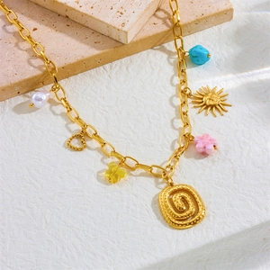 Gold spiral sun and snake pendant necklace with colorful charms on a stone background