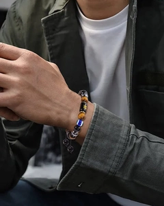 Macro detail of men's tiger eye bead bracelet with M letter and evil eye charm