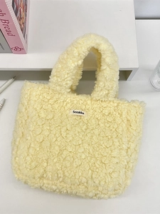 Soft light yellow plush teddy tote bag with a minimalist brand label on a desk