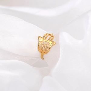 Detailed view of golden Hand of Fatima ring with hollow carving on white silk fabric