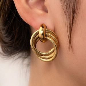 Detail view of woven gold titanium steel hoop earrings on model with high gloss finish