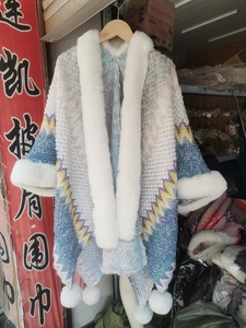 Close-up of wavy knit shawl with white faux fur collar and decorative pom-poms