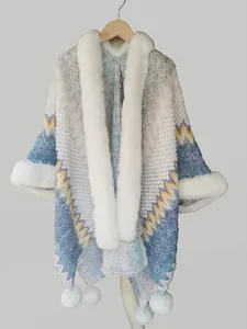 Close-up of wavy knit shawl with white faux fur collar and decorative pom-poms