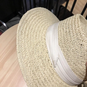 Detailaufnahme der Strohhut-Struktur mit elegantem cremefarbenem Band auf Holz