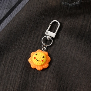 Cute sunflower resin keychain with a smiling face and orange petals on textured fabric