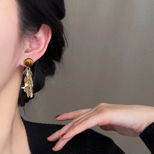 Close-up of elegant leaf tassel earrings with brown resin beads on female model