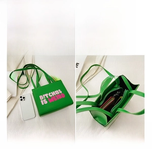 Detail view of green tote bag with pink letter print showing interior zip pocket and storage