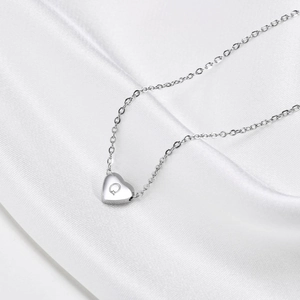 Macro shot of silver heart pendant with engraved letter Q on white silk background