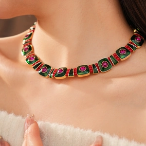 Close-up of vintage gold necklace with green enamel and red beads on a female model