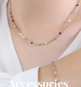 Detail of gold chain necklace and bracelet with blue and white enamel dots on a model