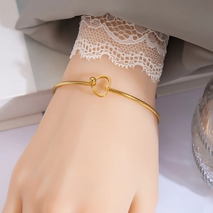 Close-up of a minimalist gold heart knot bracelet on a wrist with lace detail