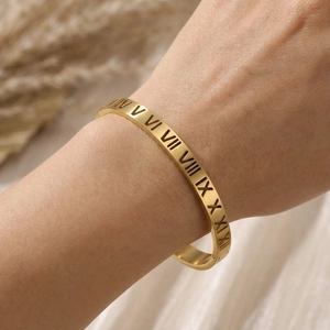 Close-up of gold titanium steel bangle with hollow Roman numerals worn on wrist