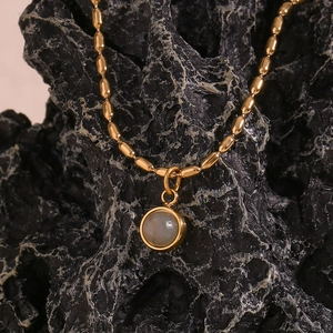 Macro detail of 18K gold-plated chain with round grey stone pendant on dark rock