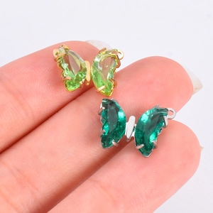 Handheld view of two zircon butterfly pendants in light and emerald green with gold frames
