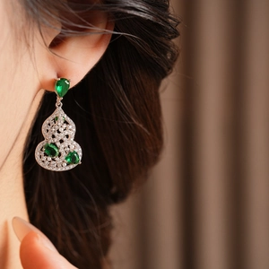 Detail of silver gourd earrings with green zircon gems worn by a model in soft light