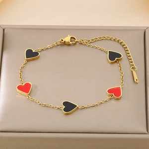Close-up of gold chain bracelet with five red and black heart charms on a beige tray