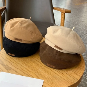 Detail of wool beret hats in neutral tones with 'Hand Made' leather labels on a wooden table