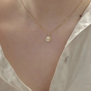 Close-up of a 14k gold plated shell pendant with a white pearl on a delicate silver chain