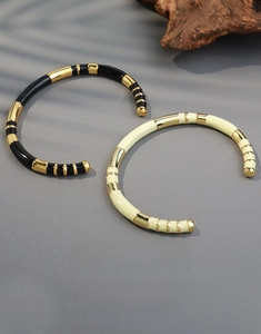Close-up of gold metal open bangles with black and beige enamel and striped texture