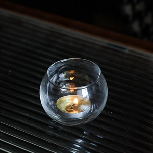 Nordic round crystal glass candle holder with lit tealight on a dark textured surface