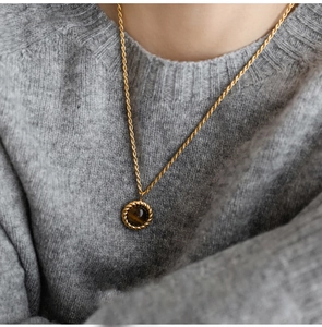 Detail of vintage gold tiger eye stone pendant on twist chain worn over a grey sweater