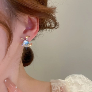 Detailed close-up of a gold-plated rabbit stud earring with a blue opal stone on model