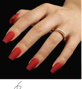 Close-up of matte red coffin nails with a pearl gold ring against a dark background