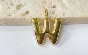 Detail of a golden puffed letter W pendant with a smooth metallic finish on a stone surface