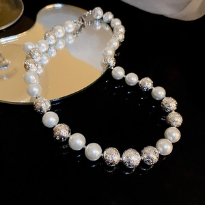 Detail shot of elegant round pearl and textured silver bead necklace on black surface