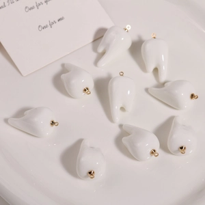 Detail of creative resin tooth charms with gold eyelet hooks in a white ceramic dish