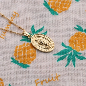 Detailed close-up of gold Virgin of Guadalupe medallion necklace on patterned fabric