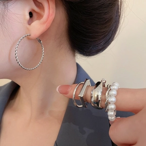 Detailed shot of twisted silver hoop earrings and stacked pearl rings on a model
