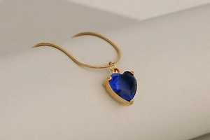 Detail of dark blue heart crystal pendant on a sleek gold snake chain necklace