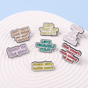 Close-up of seven colorful enamel pins with motivational quotes on a white display stand