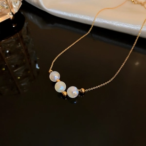 Macro shot of three iridescent pearls on a gold chain over black mirror and white silk