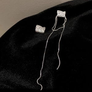 Détail de boucles d'oreilles géométriques argentées avec longues franges sur tissu noir