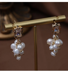 Detail of gold grape earrings with baroque pearls and sparkling zircon on a stand