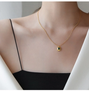 Detail of square gold pendant necklace with deep green oval crystal on woman neck