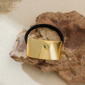 Elegant black elastic hair tie with golden rectangular metal accent on a natural stone